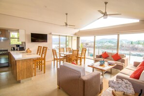 A modern kitchen with a dining area, a living room with a sofa and coffee table, and a large window offering a view of the outdoors.