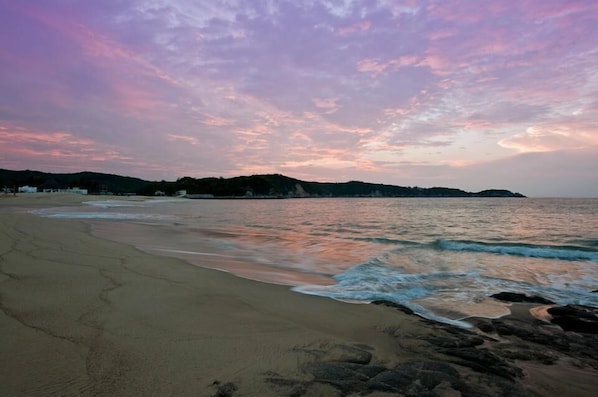A beach with a calm sea, sandy shore, and distant hills.