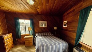 A cozy cabin bedroom with a bed, dresser, and window with curtains.