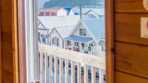 A wooden cabin with a balcony overlooking a row of houses and mountains.