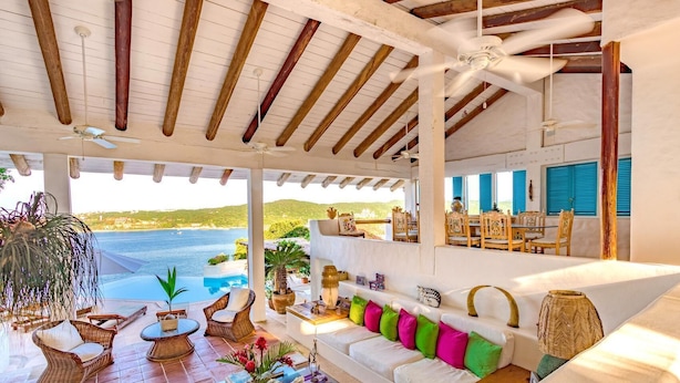 A spacious room with a large window overlooking a pool and the sea, wooden beams on the ceiling, and a white sofa with colorful cushions. - Villa Roxana (Santa María Huatulco)