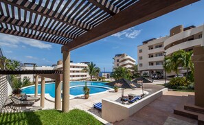 A pool area with lounge chairs, a covered seating area, and a view of the ocean.