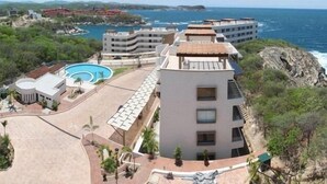 A coastal hotel with multiple buildings, a swimming pool, and a rocky landscape. - Punta Arrocito D202 (Santa María Huatulco)