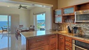 A modern kitchen with wooden cabinets, a granite countertop, and a view of the ocean. - Punta Arrocito D202 (Santa María Huatulco)
