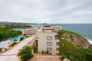 A coastal hotel with a rooftop pool, multiple balconies, and ocean views.