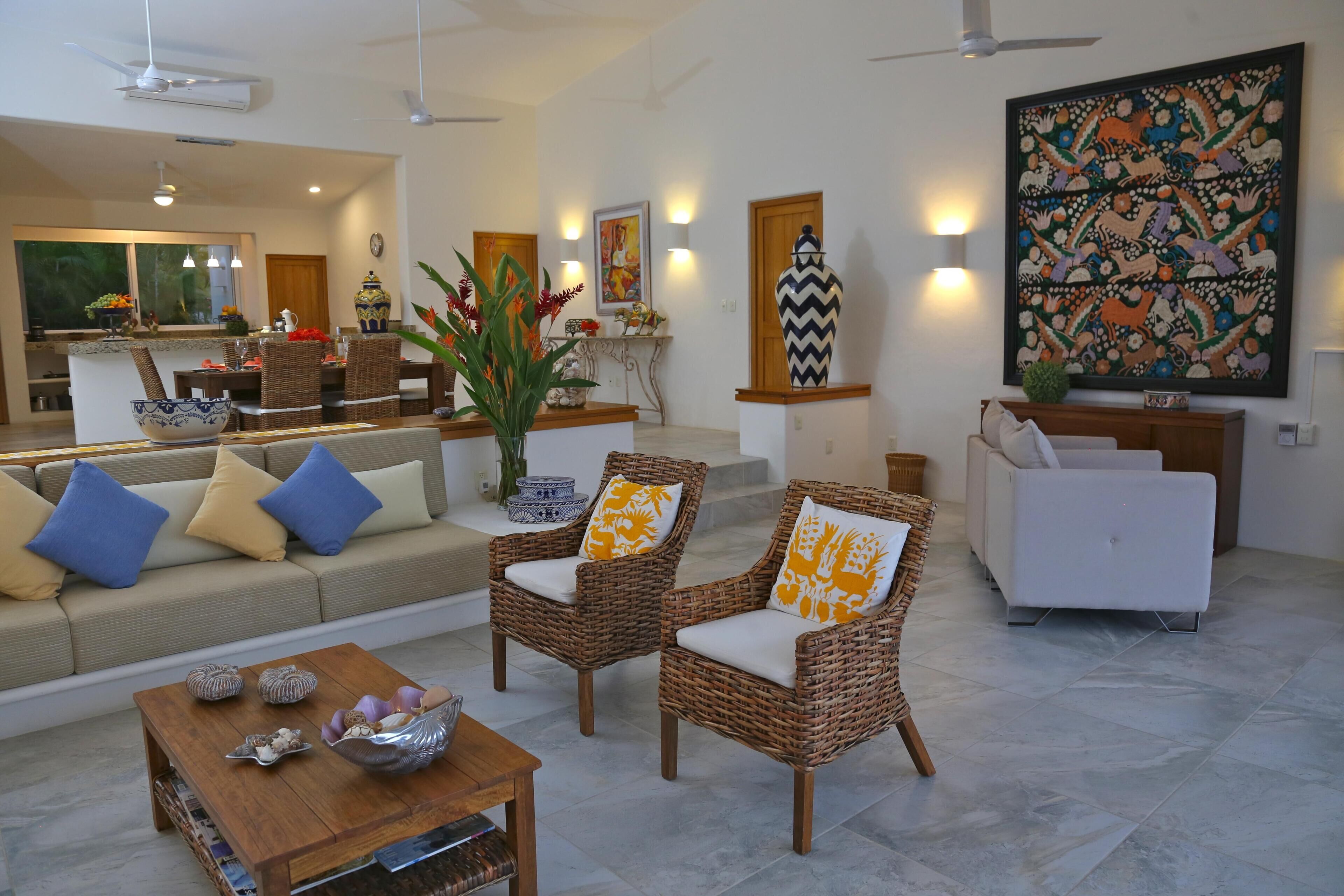 A modern living room with wicker furniture, a white sofa, and a dining area with a wooden table.