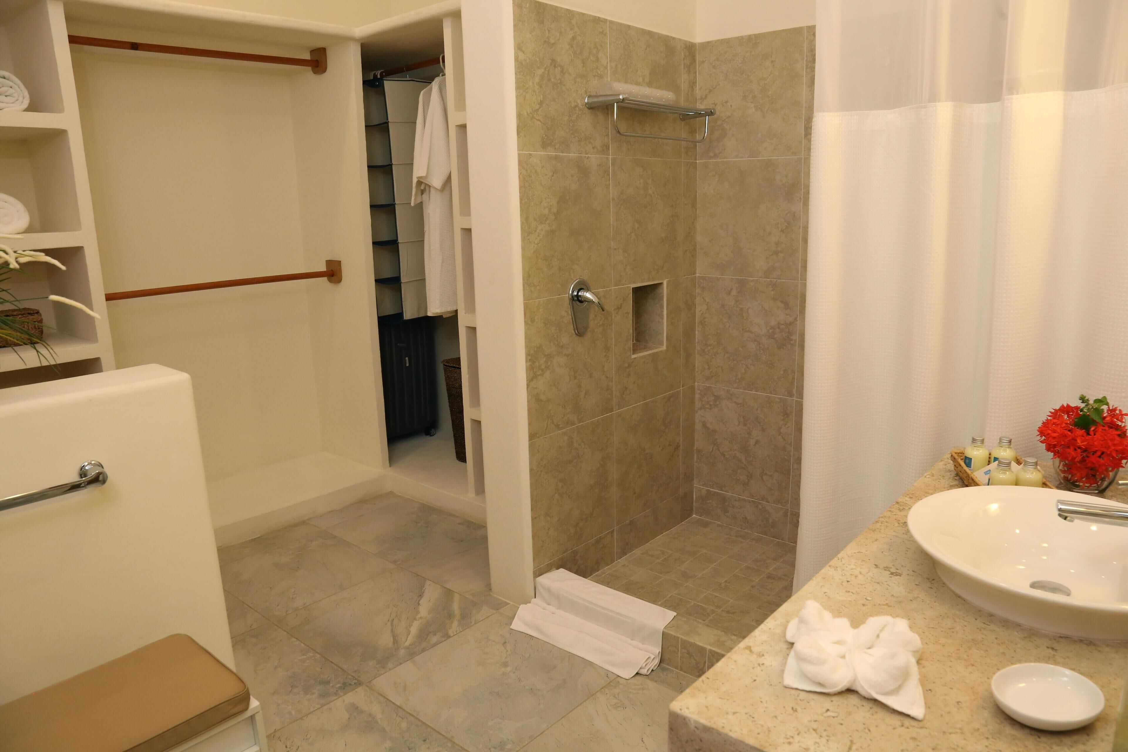 A bathroom with a beige tiled shower, a white sink, and a towel on the counter.