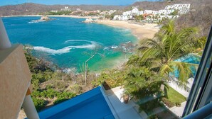 A coastal view with a beach, clear blue waters, and white buildings.