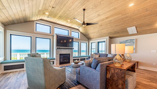 A spacious living room with a fireplace, large windows, and a view of the ocean. - Aftermath - Corolla, Ocean Sands, Oceanfront Luxury, Pool, Hot Tub, Elevator, Rec Room (Corolla)