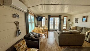 A cozy cabin interior with a wooden ceiling, a sofa, a couch, a dining table with chairs, and a television mounted on the wall. - Captain's Quarters (Bayview)