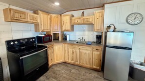 A kitchen with wooden cabinets, a stainless steel refrigerator, a black stove, and a microwave. - Captain's Quarters (Bayview)