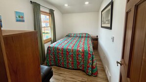 A bedroom with a bed, a wooden bench, a window with curtains, and a door. - Captain's Quarters (Bayview)