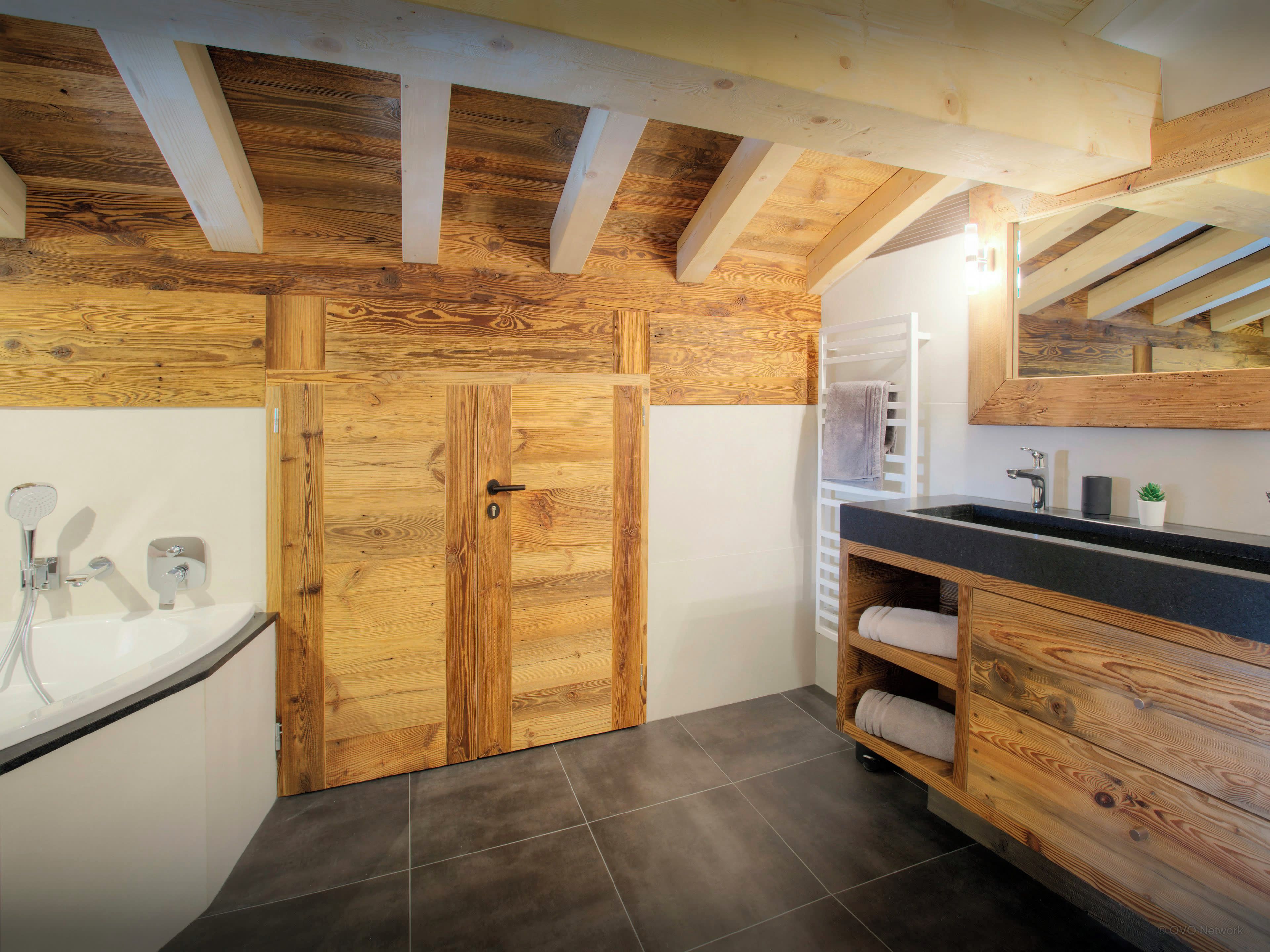 Une salle de bain avec une porte en bois, une baignoire, un lavabo avec un miroir et un porte-serviettes.