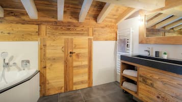 Une salle de bain avec une porte en bois, une baignoire, un lavabo avec un miroir et un porte-serviettes.