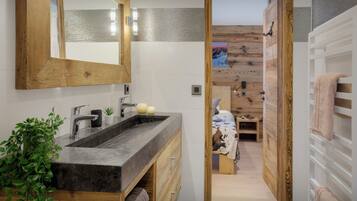 Un baño moderno con tocador de madera, un espejo grande y vistas a un dormitorio con pared de madera y una cama.