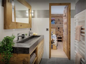 Ein modernes Badezimmer mit einem Holzkosmetikschrank, einem großen Spiegel und Blick in einen Schlafbereich mit einer Holzvertäfelung und einem Bett.