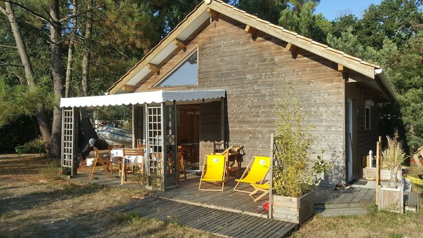 A wooden cabin with a covered porch, a boat outside, and outdoor seating. - Chalet 1 to 5 persons garden and terrace with pergola in residential park (Soulac-sur-Mer)