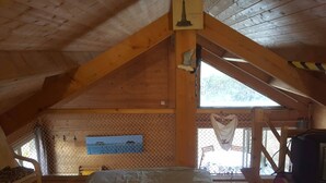 A high-ceilinged wooden room with a sloped roof, a window with a view of the outdoors, and a bed with a white sheet. - Chalet 1 to 5 persons garden and terrace with pergola in residential park (Soulac-sur-Mer)
