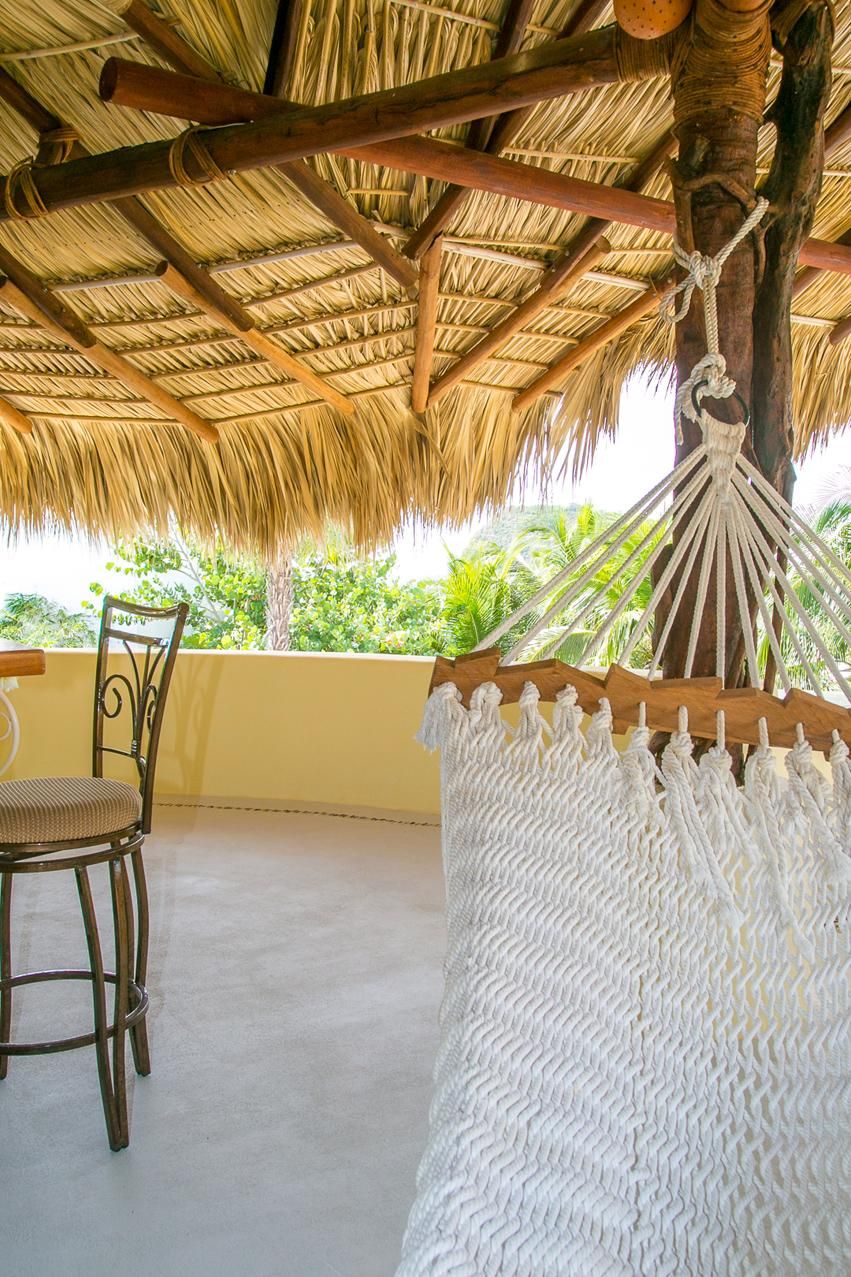 Una hamaca bajo un techo de paja, una silla de mimbre y vistas al verdor.