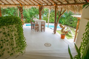 Ein überdachter Außenbereich mit Pool, Holzmöbeln und üppiger Bepflanzung.