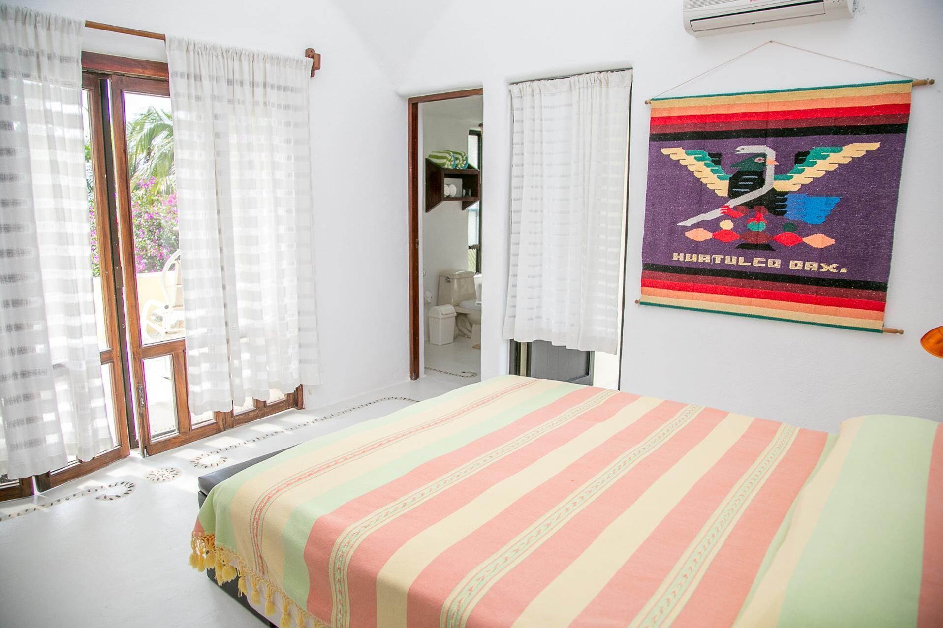 A bedroom with a bed, curtains, a mirror, and a wall hanging.