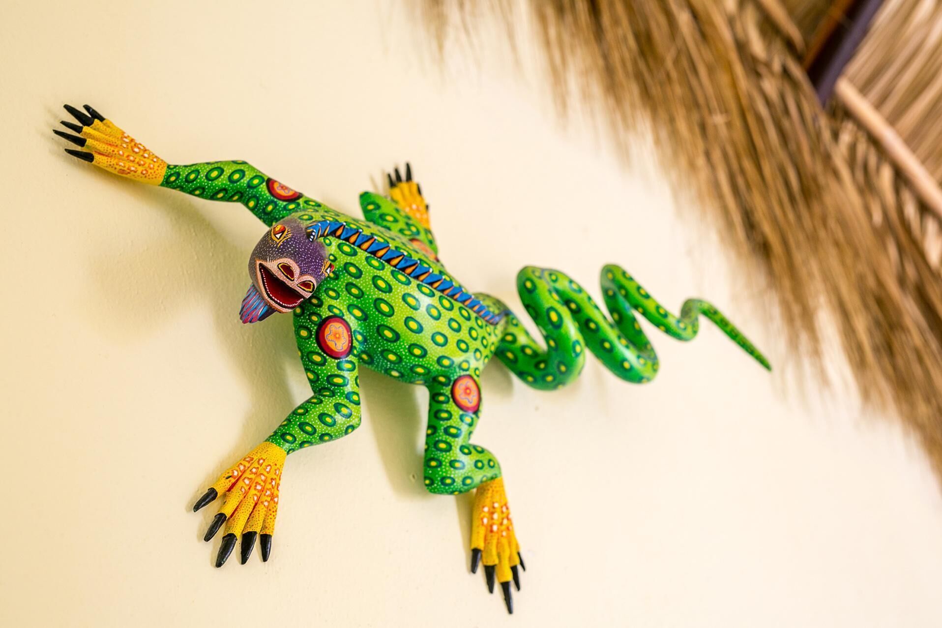 Une sculpture colorée et ornée de motifs représentant un lézard ou une grenouille, placée sur un mur uni.