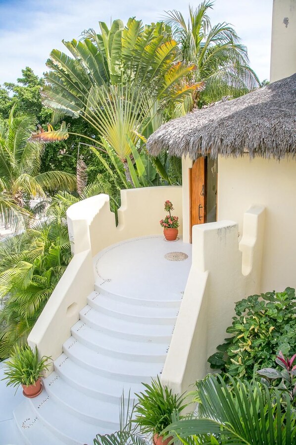 A circular staircase leading to a thatched-roof structure surrounded by lush tropical plants. - Villa Flory (Santa María Huatulco)