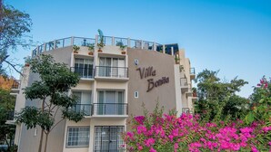A multi-story building named "Villa Bonita" with balconies, potted plants, and a garden with pink flowers.