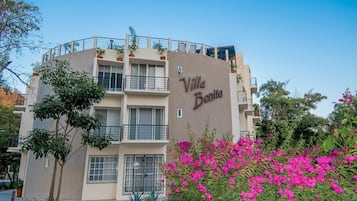 A multi-story building named "Villa Bonita" with balconies, potted plants, and a garden with pink flowers.