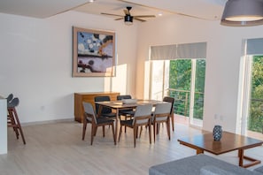 A spacious dining area with a wooden table and chairs, a ceiling fan, and a large window with a view of greenery. - Villa Bonita PH (Santa María Huatulco)