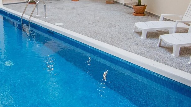 A multi-level indoor pool area with a clear pool, potted plants, and white lounge chairs.