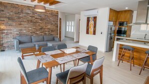 A modern living space with a dining area, a sofa, and a kitchen.