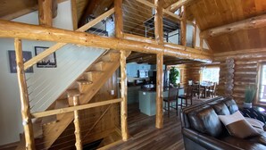 Interno di una baita in legno con una scala, una zona cucina e un soggiorno con divano in pelle.