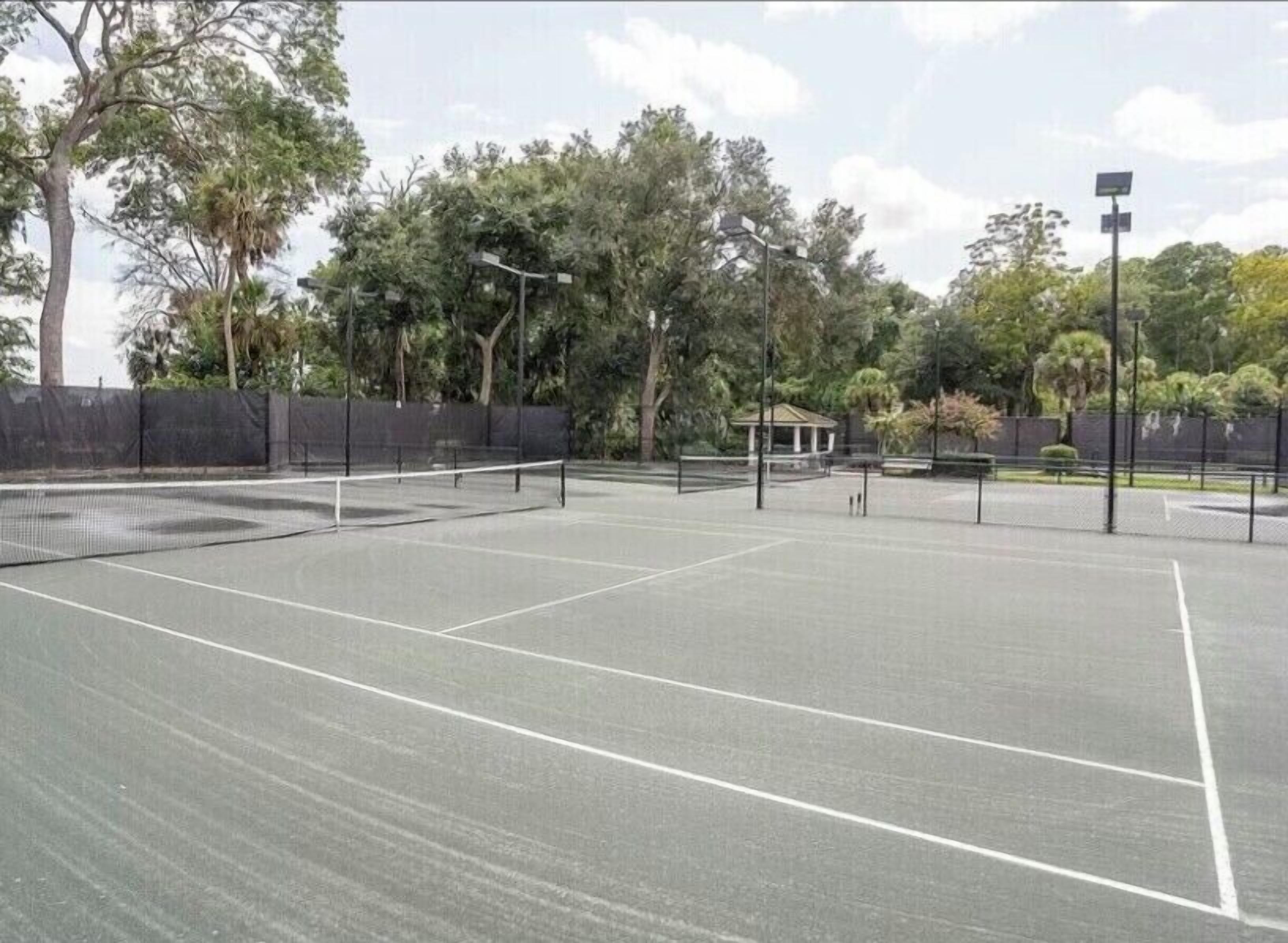Ein Tennisplatz im Freien mit Netz, umgeben von Bäumen und einem Zaun.