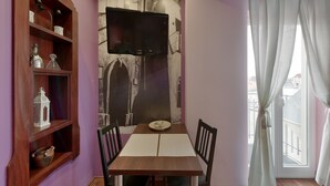Ein Essbereich mit einem Holztisch, Stühlen, einem an der Wand befestigten Fernseher und einem Fenster mit Vorhängen.