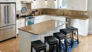 A modern kitchen with white cabinetry, a large island with bar stools, stainless steel appliances, and pendant lighting.