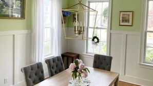 A dining room with a wooden table, six upholstered chairs, a chandelier, and a vase with flowers.