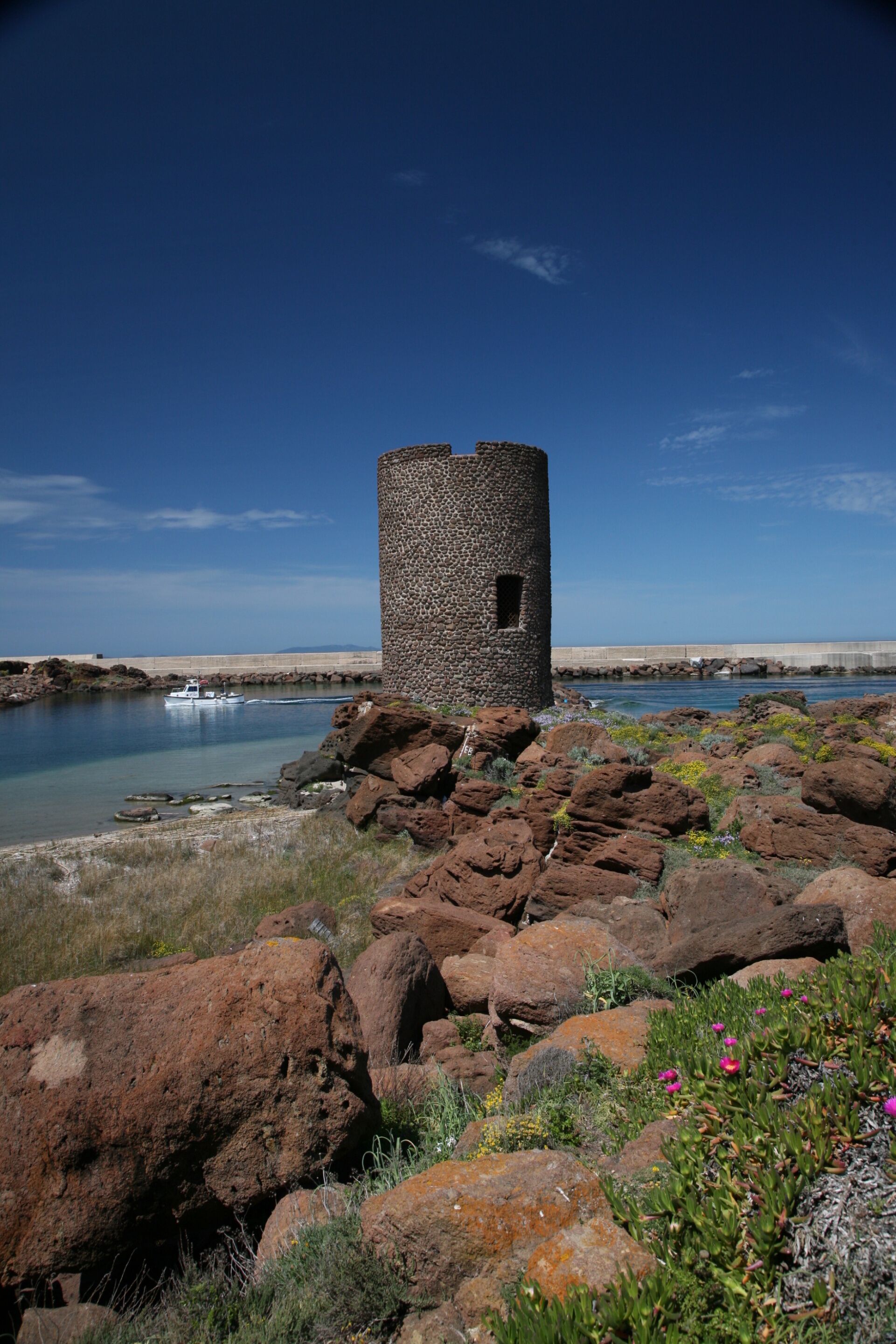 Una torre di pietra affacciata su un mare calmo, con un terreno roccioso e scarsa vegetazione.