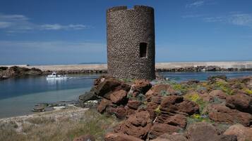 Una torre di pietra affacciata su un mare calmo, con un terreno roccioso e scarsa vegetazione.