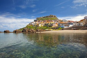 A coastal town with colorful buildings, a clear beach, and a fort on a hill.
