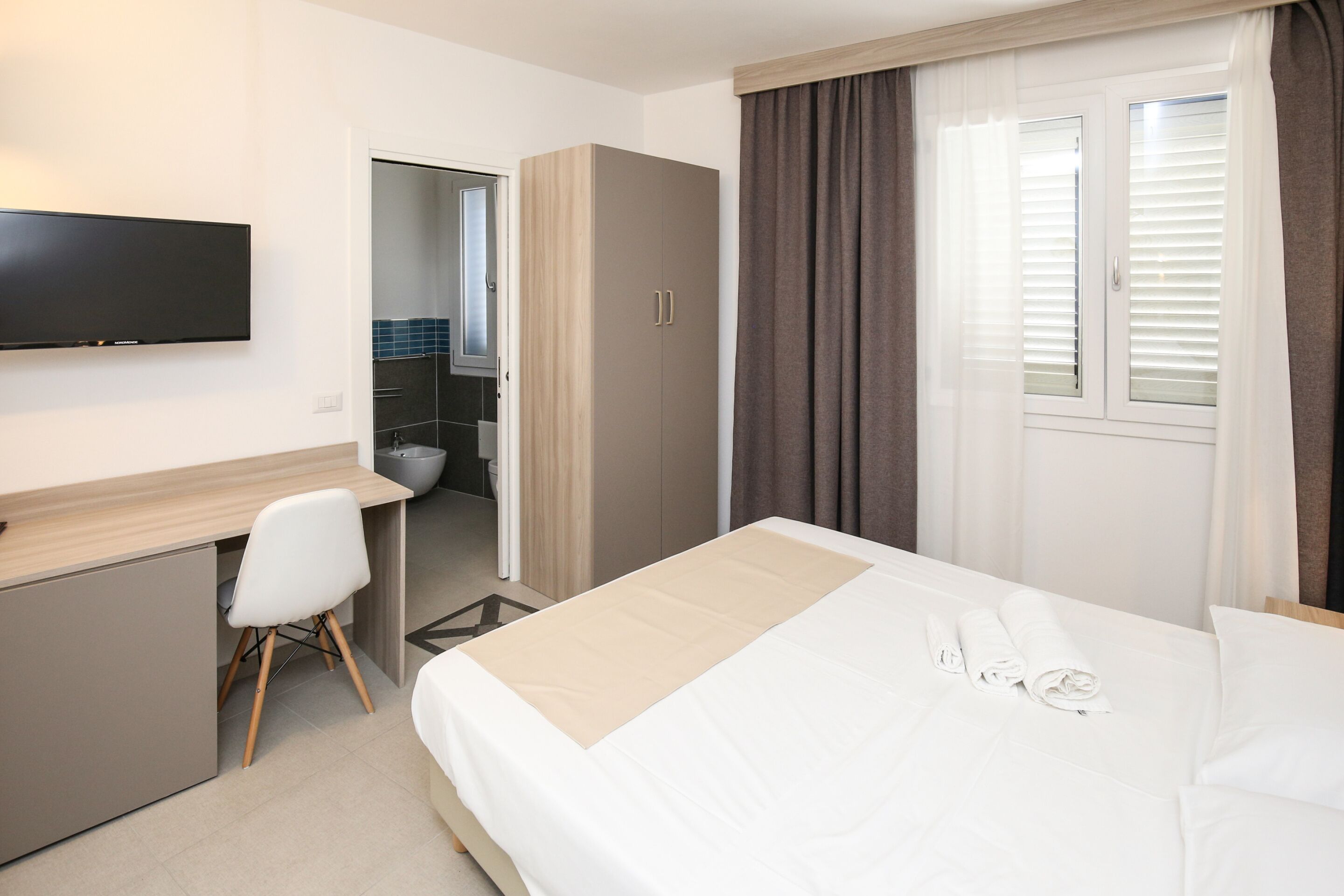 Habitación de hotel con cama, escritorio, silla, armario y televisión.