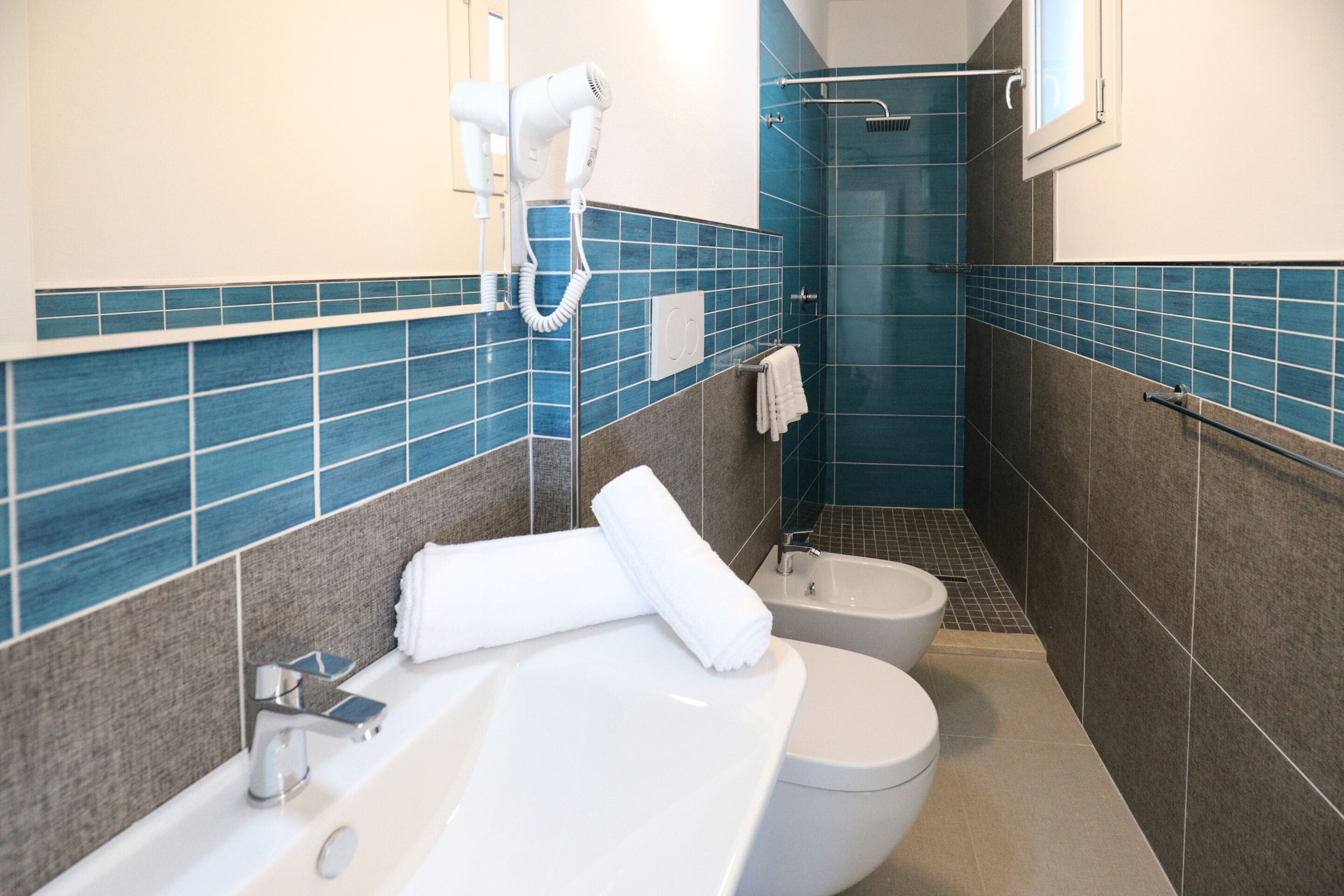 A bathroom with a bathtub, two toilets, a shower, and a hairdryer on the wall.