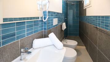 A bathroom with a bathtub, two toilets, a shower, and a hairdryer on the wall.