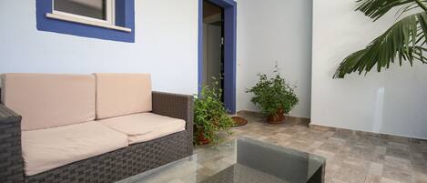 A room with a beige sofa, a glass coffee table, and potted plants.
