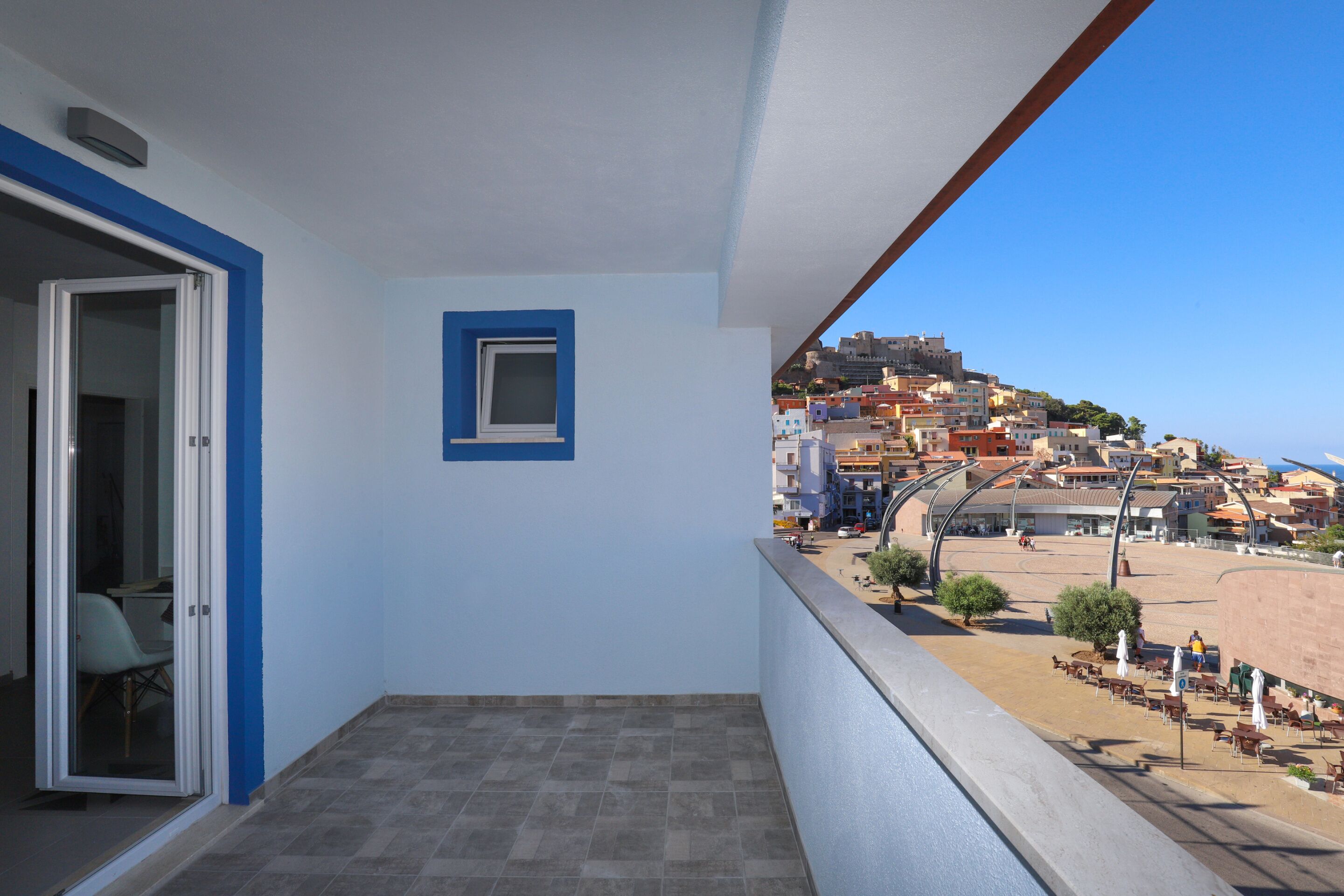 Ein Balkon mit freiem Blick auf eine Küstenstadt, eine Tür, die zu einem Zimmer führt, und ein kleines Fenster.
