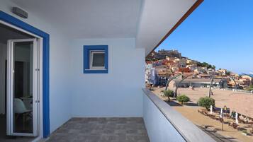 Ein Balkon mit freiem Blick auf eine Küstenstadt, eine Tür, die zu einem Zimmer führt, und ein kleines Fenster.