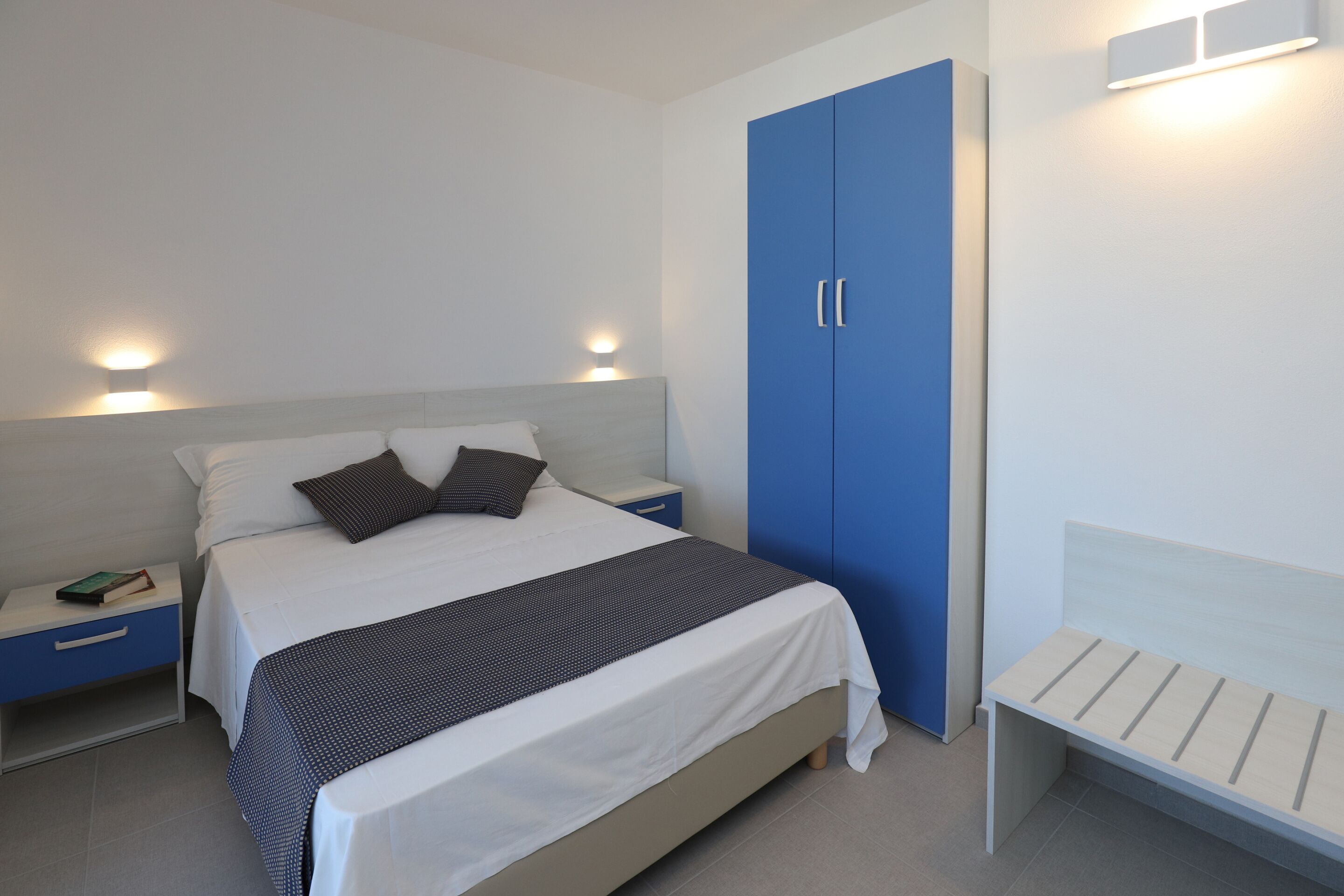Een slaapkamer met een bed, nachtkastjes, een garderobe en een bankje.