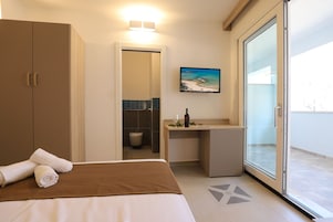 A hotel room with a bed, a desk, a bathroom, and a sliding glass door to the outside.