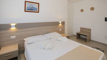Una habitación de hotel moderna con cabecera de madera, cama con ropa de cama blanca, mesita de noche con lámpara y un pequeño banco de madera.