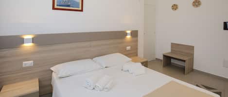 A modern hotel room with a wooden headboard, a bed with white linens, a bedside table with a lamp, and a small wooden bench.